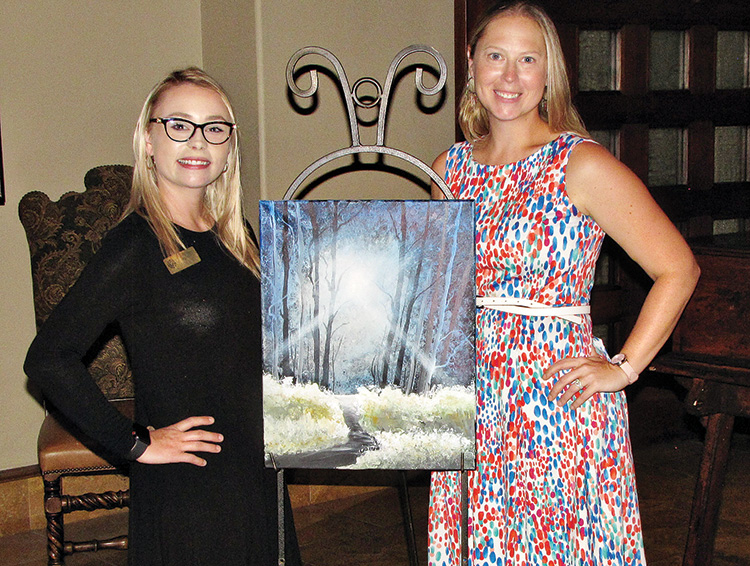 Assistant Event Coordinator Sabrina Minney (left) and Event Coordinator Crystal Thomas pose with the painting created for the July Paint and Wine event.