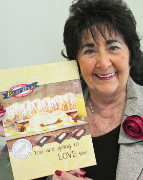 Carol Phillips of our Friendship Committee holds a small poster for Butter Braids.