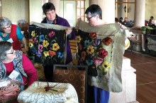 Barb Mauer and Karen Bogadi hold up their rugs for viewing.