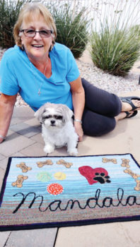 Donna Holbeck and long-time best friend, Mandalay, enjoy a few of the dog’s favorite things designed into a hand-hooked wool rug. Dog biscuits, balls for chasing and “squeaking” and a paw print over a heart create a unique memory for years to come.