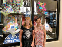 Quilters Mary Sheldon and Irene Lukes display several charity quilts in a window of the Creative Arts Center.