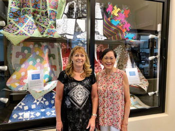 Quilters Mary Sheldon and Irene Lukes display several charity quilts in a window of the Creative Arts Center.