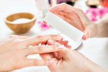 Closeup shot of a woman in a nail salon receiving a manicure by a beautician at nail salon. Woman using a buffer for file nail. Shallow depth of field with focus on nailfile.