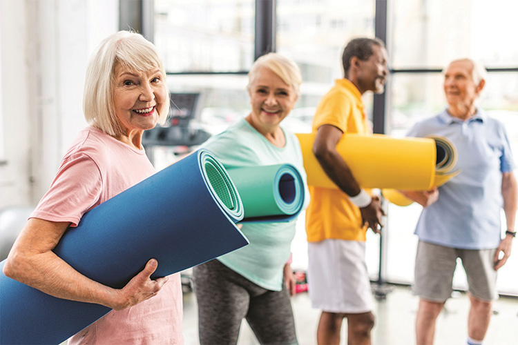 selective focus of senior sportswoman holding fitness mat and her friends standing behind at gym