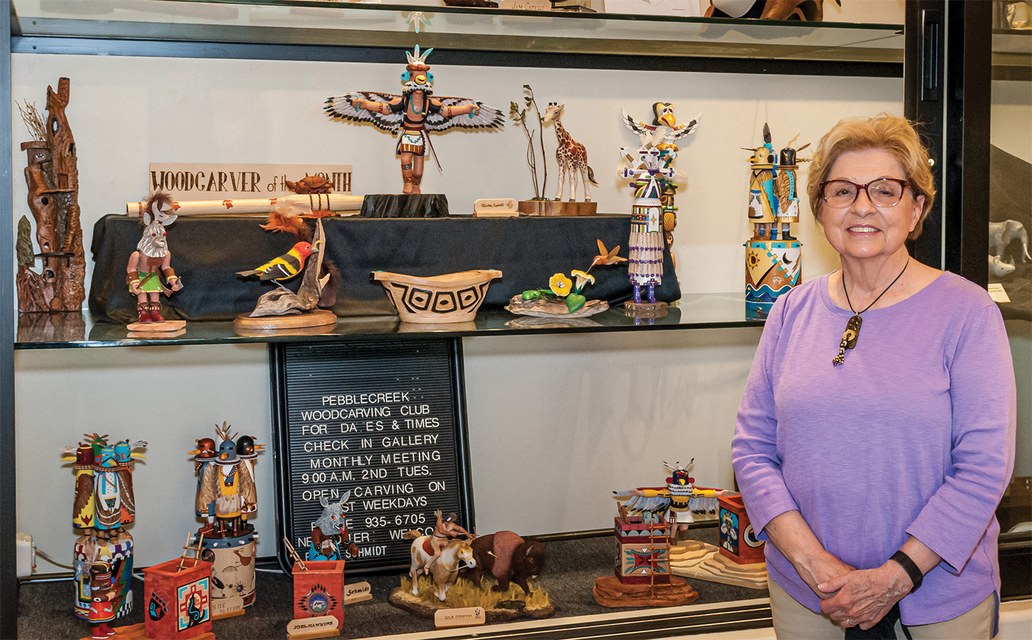 Elaine with several of her carvings on the middle shelf of the carving club's display window in the Creative Arts Center.